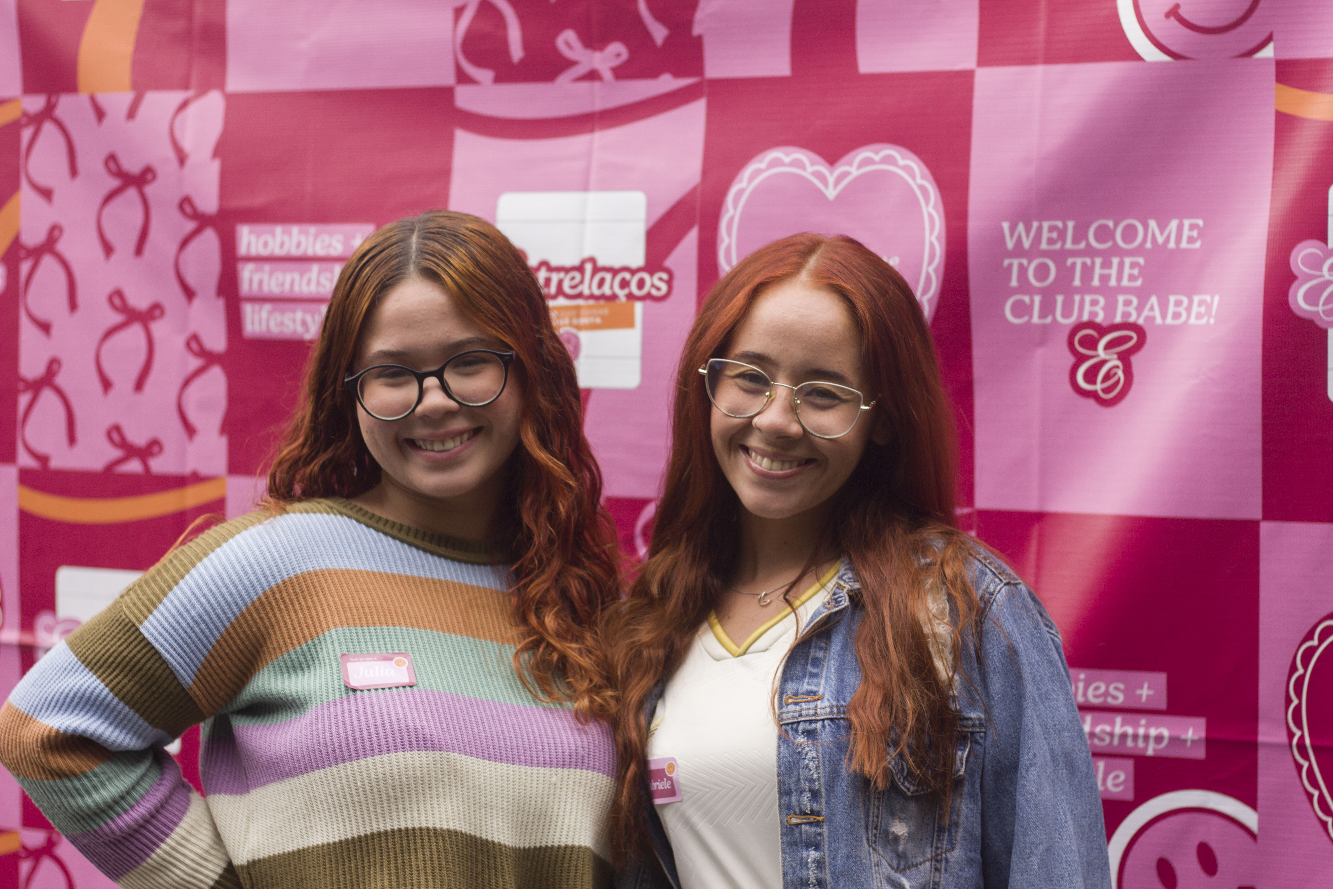Duas participantes do Entrelaços sorrindo em frente ao painel da marca